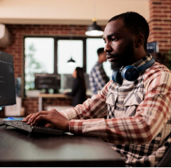 Man with headphones typing at a desktop computer in an office